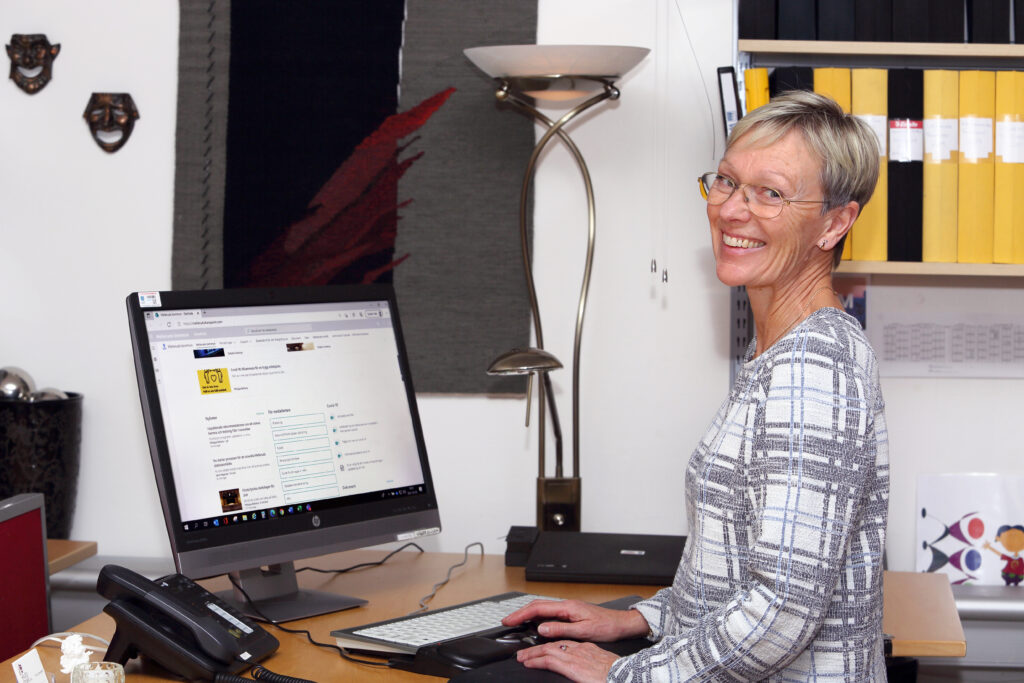 En kvinna i kort ljust hår står framför en dator och ler in i kameran. Kulturbruket på Dal.