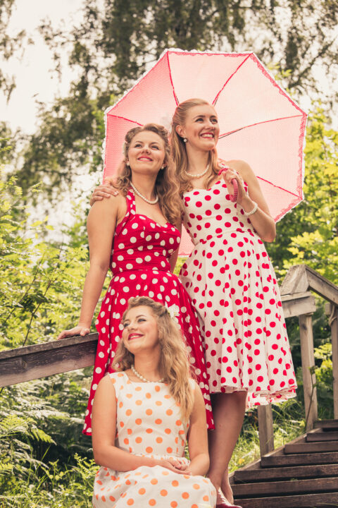 The Hebbe sisters poserar under ett rosa paraply i prickiga klänningar.