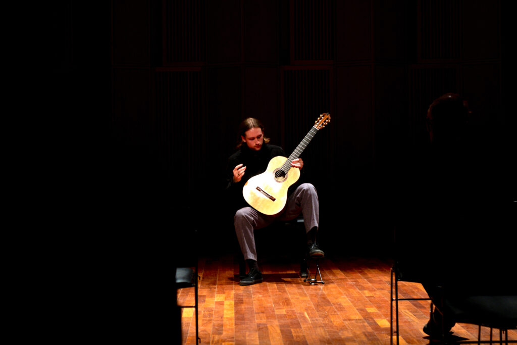 Jon Svenungsson sitter i en spotlight på scen med sin gitarr.