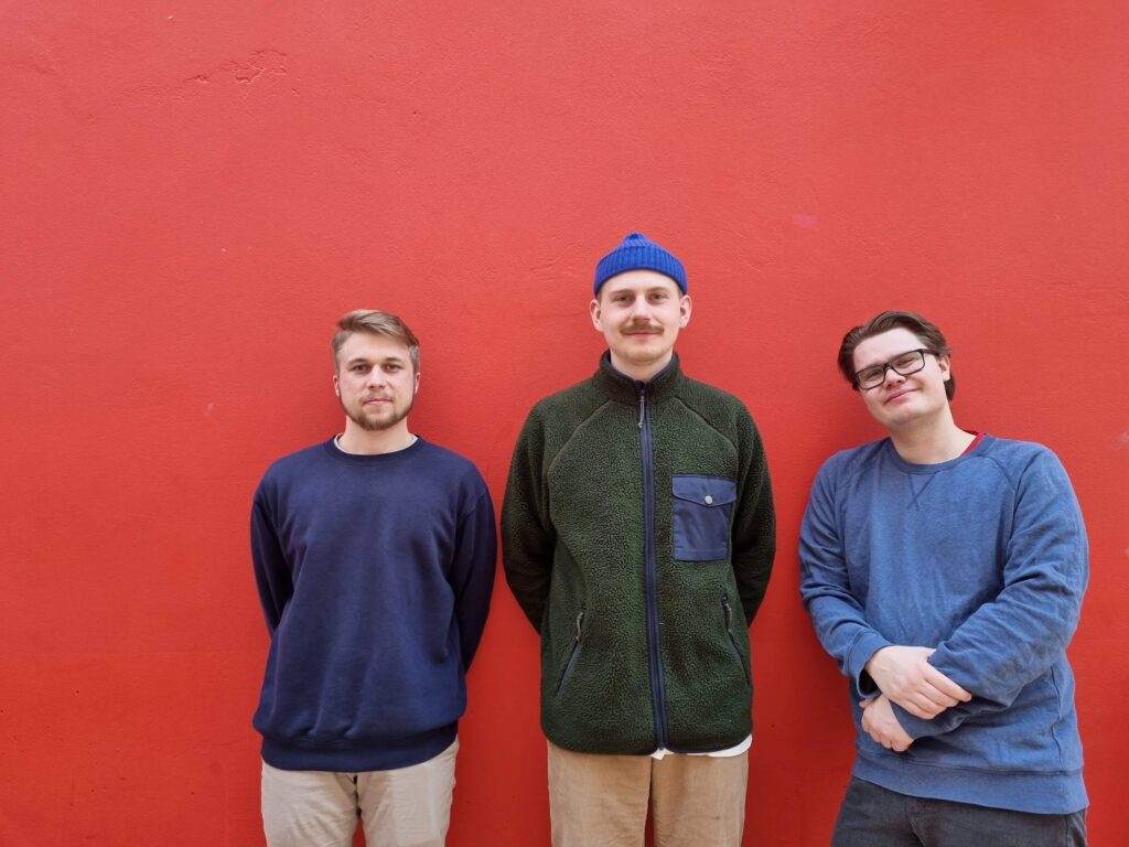 Tre killar står framför en röd vägg.