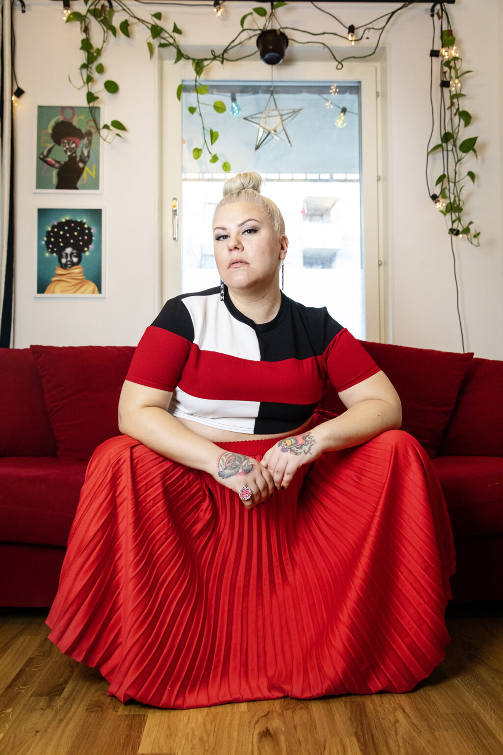 Karin Kajjan Andersson sitter i en lång röd kjol med utbredda knän i en röd soffa. Fotot är taget lite underifrån.
