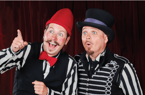 Två clownklädda personer står framför en röd sammetsridå med intensiva ansiksuttryck.