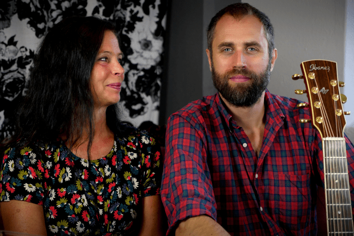 Åsa Johansson i blommig blus och Johan Ludvig Rask i rutig skjorta. Johan håller en gitarr.