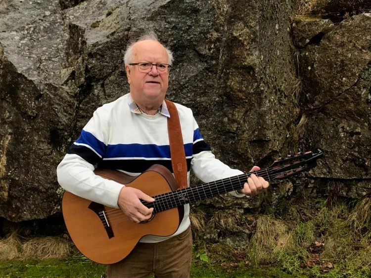 Lars Nilsson står framför en klippvägg med sin gitarr.