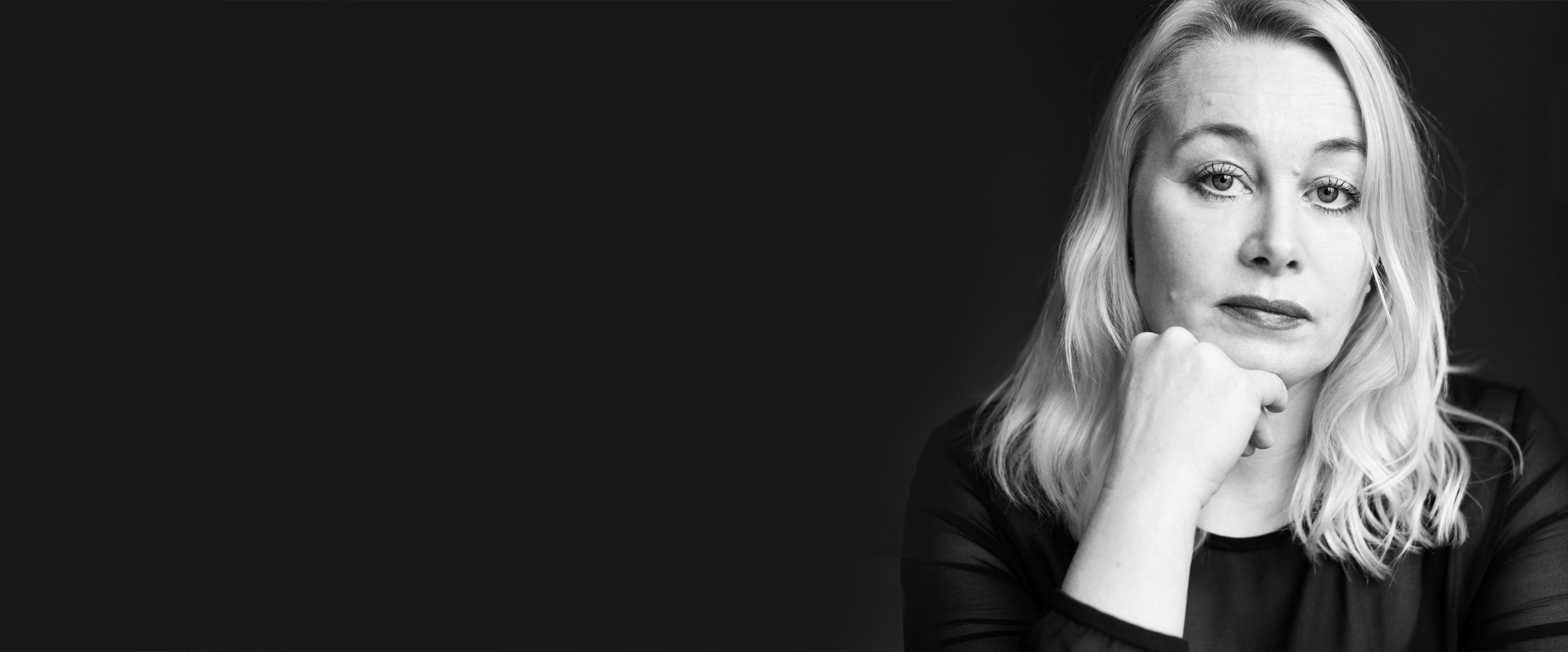 Ann Heberlein i ett svartvitt, allvarligt, porträtt mot en svart bakgrund.
