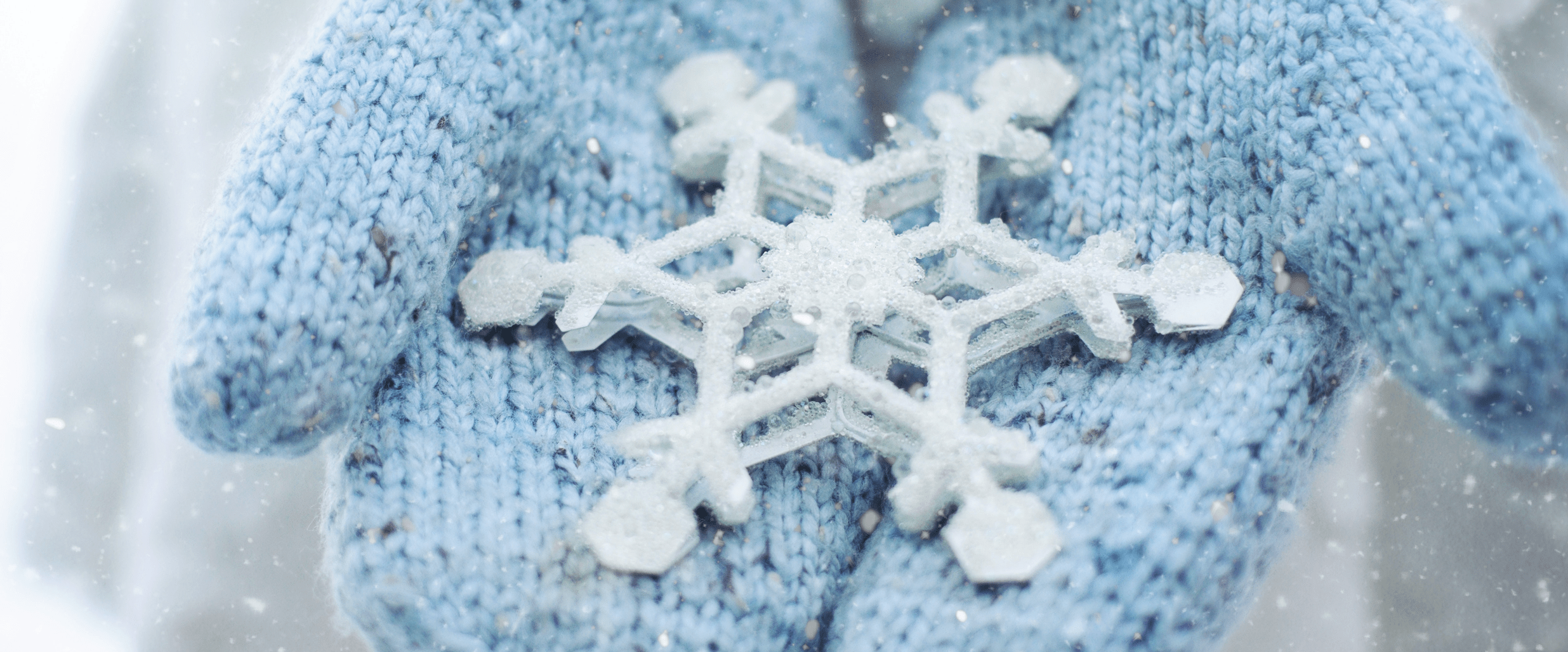 En stor snöflinga ligger i ett par kupade händer med ljusblå stickade vantar.