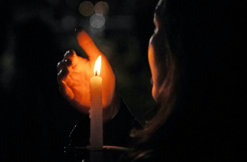 En person håller sin hand runt ett ljus i mörkret.
