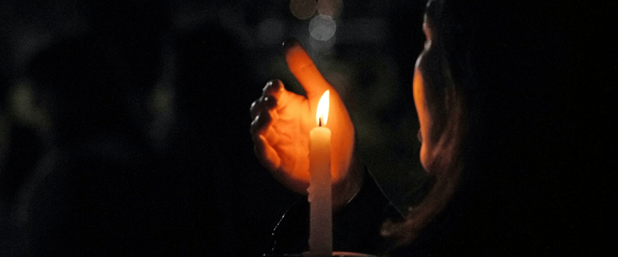 En person håller sin hand runt ett ljus i mörkret.