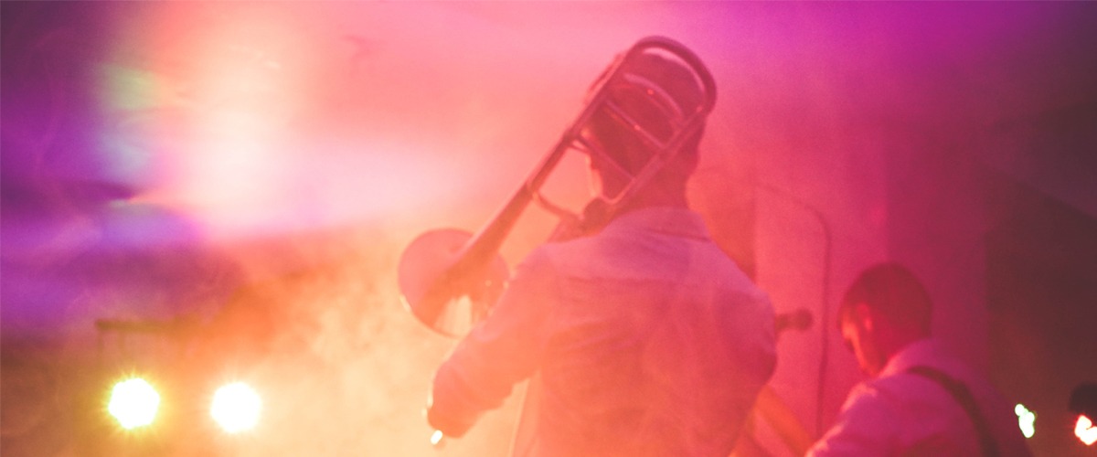 En trombonist spelar på en rosa/orange upplyst, rökig scen.