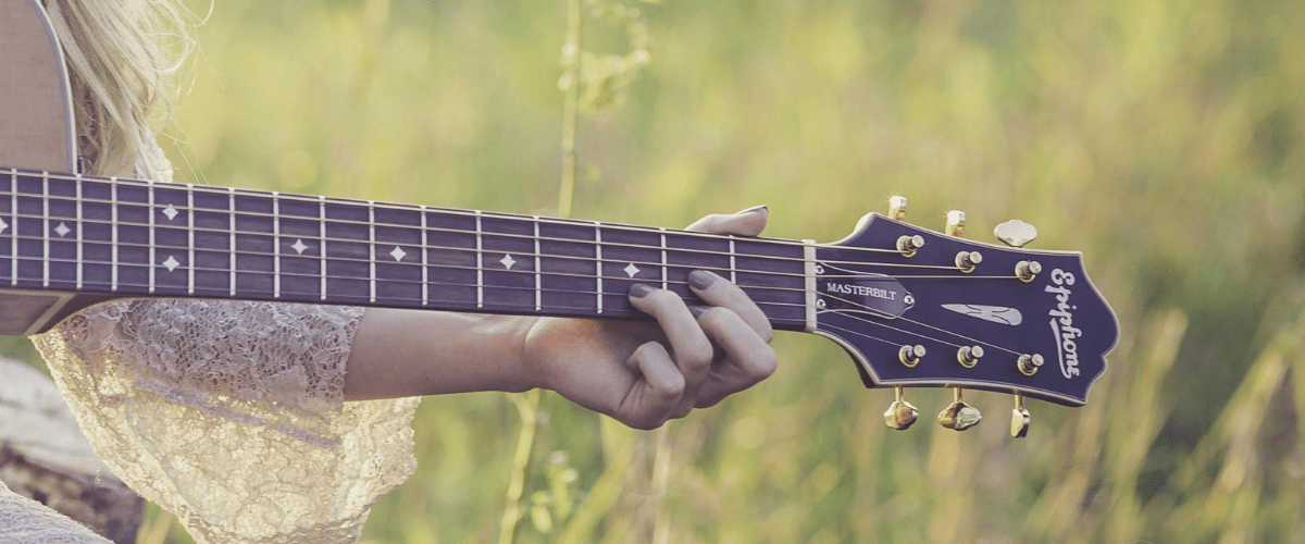 En person i spetsklänning spelar gitarr på en grön äng.