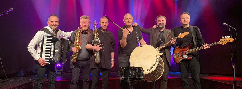Andra generationens medlemmar med sina instrument på en rosalila upplyst scen.