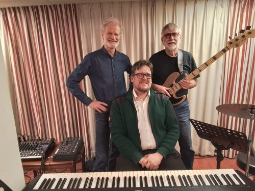 Fredrik Almqvist och hans två kompanjoner bakom en keyboard, en av dem håller i en bas.