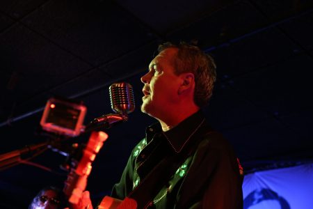 Dick Johansson står på scen och sjunger och spelar gitarr.