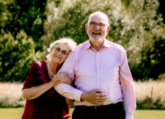 Lena och Paul Forsén står ute i sommargrönskan, leendes, iklädda rosa.