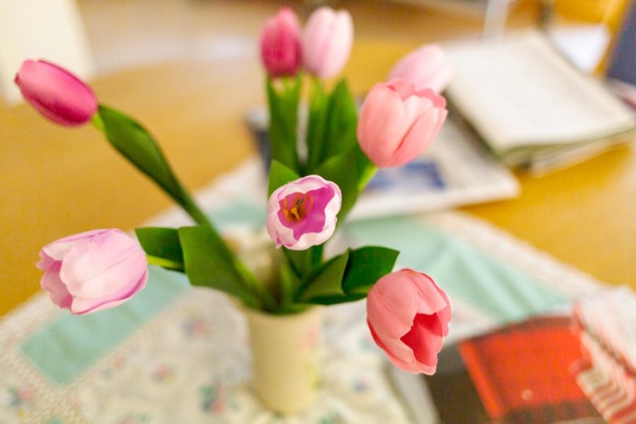 En vas med rosa tulpaner på ett bord med lite block och en duk.