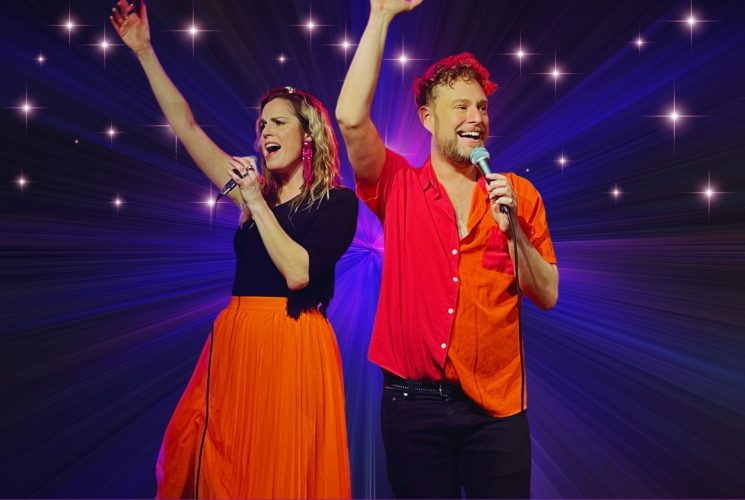 Pernilla och Robin sjungandes klädda i svart och rött framför en stjärnfylld bakgrund.