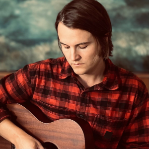 Samuel i rödrutig skjorta tittar ner på gitarren han spelar på.