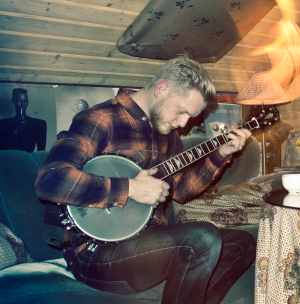 Treehugger sitter i en soffa under ett snedtak och spelar banjo.