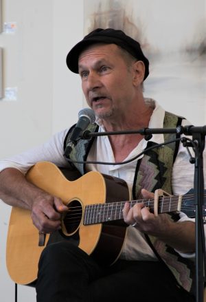 Alban Faust sitter framför en mick och spelar gitarr. Han har på sig en svart basker.