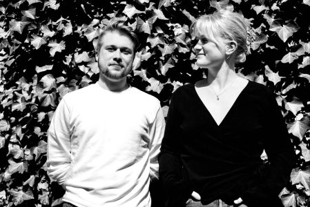 Simon Bertilsson och Lif Magnusdottir står framför en vägg av murgröna, de ler och Lif tittar på Simon. Det är ett svartvitt foto.
