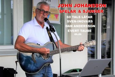 John Johansson sjunger i en mikrofon och spelar gitarr. Framför honom står en laptop.